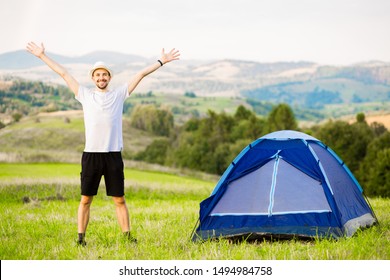 Young Man With Hands Up Camping Tent Facing Amazing Views Of Mountain With Blue Sky.