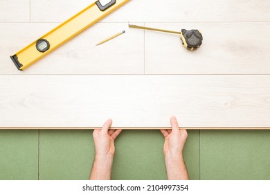 Young Man Hands Laying Light Color Laminate On Green Natural Wood Fiber Insulation Board. Flooring Installation On Fibreboard Underlay. Repair Work Of Home. Renovation Process. Closeup. Top Down View.