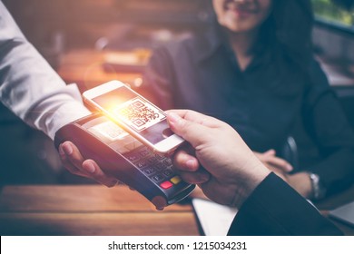 Young man hands are Smartphone to scan a QR CODE filing from a credit card reader to pay for food and beverages in restaurants which have a romantic atmosphere by the Asian girls are sitting together. - Powered by Shutterstock - Get 15% off with code: PIKWIZARD15
