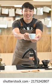 A Young Man Handsome Asian Barista Serving Coffee In A Coffee Shop With A Blurry Cup Of Coffee.