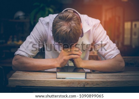 The young man handsome caucasian Americans handsome man sitting with hands clasped in prayer for blessings from God. A Bible rested on a wooden table with copy space.