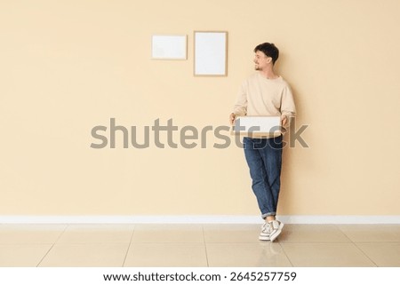 Young man hanging blank frames on beige wall