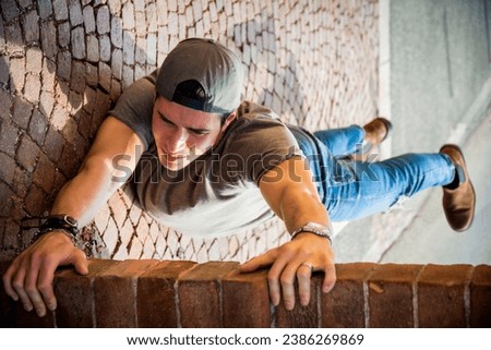 A young man hanging from a brick wall. Optical illusion shot