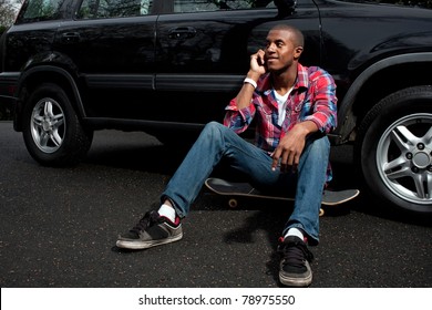 A young man hanging out sitting on his skateboard near his vehicle as he talks on his smartphone. - Powered by Shutterstock