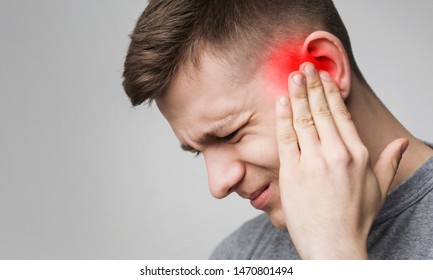 Young man has sore ear, suffering from otitis, touching his inflamed head, close up, empty space
