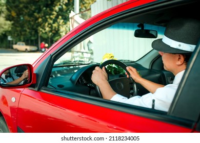 Young man in a hat driving a car. On the dashboard of the car lies a bouquet of white-yellow flowers. - Powered by Shutterstock