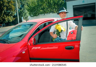 A young man in a hat gets out of the car. In the hands of a man is a bouquet of white-yellow flowers. - Powered by Shutterstock