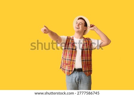 Young man in hat pointing somewhere on yellow background