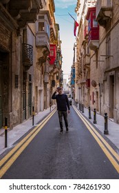 young man with hat walking at the Typical narrow streets with colorful balconies in Valletta , Malta 