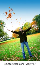 Young man having fun throwing up piles of autumn leaves .
