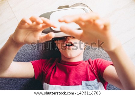 Young man having fun with virtual reality goggles technology lying on sofa at home. Astonished boy gesticulates wearing vr headset. Tech, modern lifestyle and joyful youth concept. Focus on teen mouth