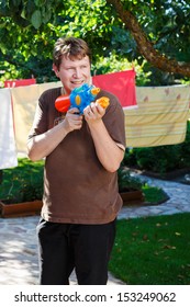 Young Man Having Fun With Water Gun In Summer Garden