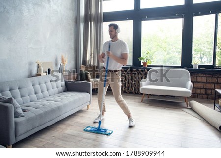 Young man having fun while cleaning his flat.