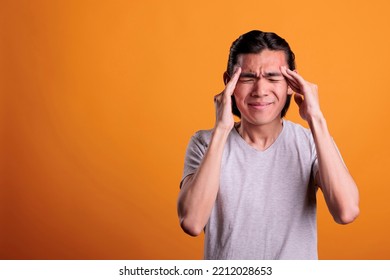 Young Man Having Headache, Touching Temples With Fingers. Exhausted Asian Teenager With Closed Eyes Suffering From Painful Migraine Symptoms, Overworked Stressed Person Feeling Unwell