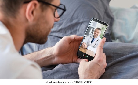 Young Man Having Online Consultation With Doctor On Smartphone, Using Telemedicine App On Bed, Panorama. Male Patient Communicating To His Physician On Mobile Device From Home