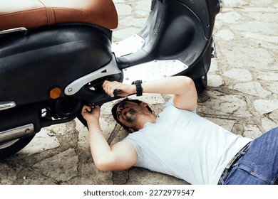 Young man having problems with the motorbike on the road. Man under the motorcycle trying to fix the problem of the motorcycle due to a breakdown. Road motorcycle insurance concept - Powered by Shutterstock