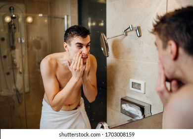 Young man having a shaving daily beard grooming routine,applying aftershave lotion.Allergic itchy rash burn reaction to hygiene skin care product.Facial hair removal.Shaving for work.Beard trim shave