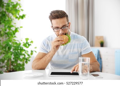 Young man having snack while working with tablet computer in kitchen