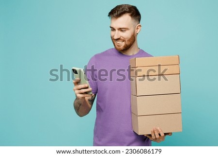 Young man he wears purple t-shirt hold in hand use mobile cell phone stack cardboard blank boxes isolated on plain pastel light blue cyan background studio portrait. Tattoo translates life is fight