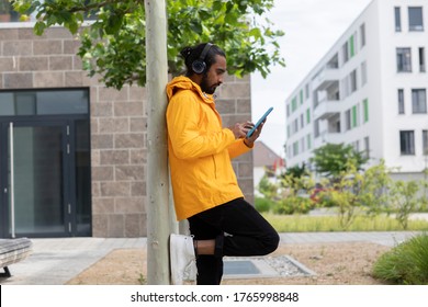 Young Man With Headphone And Tablet And Yellow Jacket Near A Tree