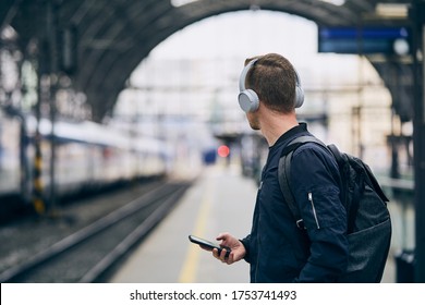 Young man with headphones listening music and waiting for train at railroad station.  - Powered by Shutterstock