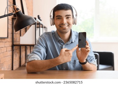 Young man with headphones pointing at mobile phone in office - Shutterstock ID 2365082715