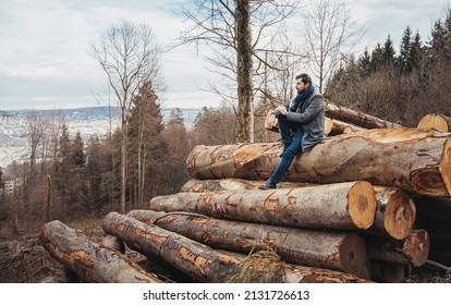 Young man with heavy clothing watching over Zurich from a height in Uetliberg while sitting on logs in an overcast winter day