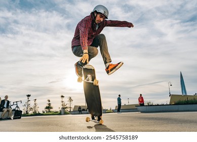 Young man in a helmet jumps on a longboard at a skate park, lit by the setting sun, showcasing his skills in an urban cityscape - Powered by Shutterstock