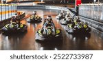 Young man in a helmet leading a group of racers in a go-kart race on an indoor track.