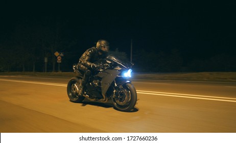 Young Man In Helmet Riding Fast On Modern Black Sport Motorbike At Evening City Street. Motorcyclist Racing His Motorcycle On Night Empty Road. Guy Driving Bike. Concept Of Freedom And Hobby. Close Up