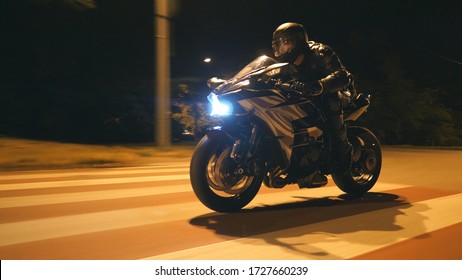 Young Man In Helmet Riding Fast On Modern Black Sport Motorbike At Evening City Street. Motorcyclist Racing His Motorcycle On Night Empty Road. Guy Driving Bike. Concept Of Freedom And Hobby. Close Up