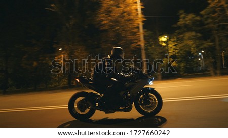 Young man in helmet riding fast on modern sport motorbike at evening city street. Motorcyclist racing his motorcycle on night empty road. Guy driving bike. Concept of freedom and hobby. Side view.
