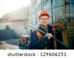 A young man in a helmet worker standing with a hammer on the shoulder