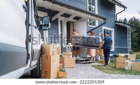 Young Man Helping a Delivery Service Worker to Bring a Modern Couch Into Their New House. Pregnant Female Opens the Door to Let Them Through. Young Family Moving to Their New Home.