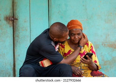 Young Man Helping An Elderly African Woman Plug In Earphones