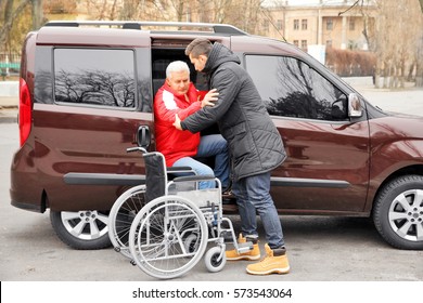 Young Man Helping Handicapped Man To Sit In Wheelchair