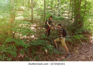 Young Man Helping His Woman To Step Down On The Steep Hill In The Forest While They Hiking Through Nature. Couple Nature Lovers In The Woods Spending Holiday Like Hikers. With Film Grain