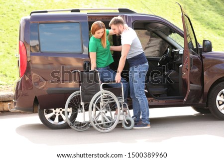 Young man helping woman to get out from van into wheelchair outdoors