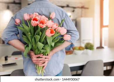 The young man is hiding flowers behind their backs to his girlfriend at home. - Powered by Shutterstock