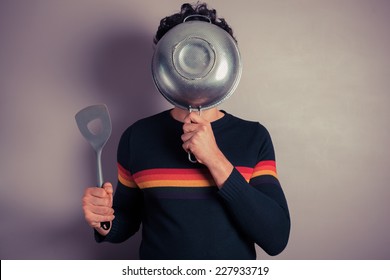 A young man is hiding his face behind a colander