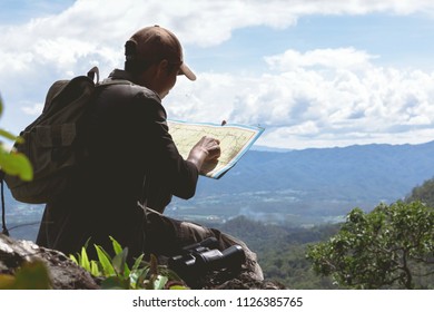 Young man hiker holding a map on a top of mountain