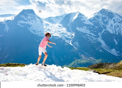 Young Man Hiking In Alps Mountains, Austria. Teenager Playing Snow Ball Fight On Snowy Mountain Peak On Warm Sunny Spring Day. Summer Family Vacation. Teen Boy On Hike Trail To Top. Outdoor Fun.


