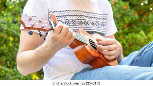 Young Man Hipster Play Ukulele Musical Instrument Outside Relax Among The Nature