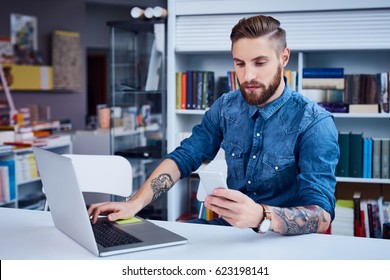 Young man, hipster using his smart phone and laptop in library
