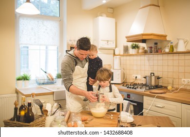 A young man and his children are preparing flavored cookies or pizza in a spacious white kitchen. Dad teaches his children to cook. Joint pastime with family.