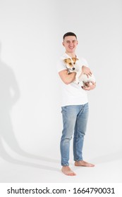 Young Man With His Dog At Studio. Young Owner Hugs His Pet. Young And Beautiful Man Holding His Dog In His Arms With Love And Playing With Him, Against A White Background