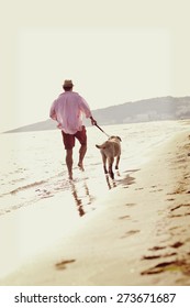 A Young Man With His Dog Walking On The Beach