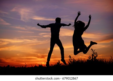 A young man with his girlfriend jump on background sunset silhouette.
