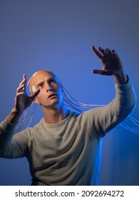 A young man with his head entangled with wires, pulls his hands up, electrical contacts on his bald head, signals to the brain. Neurointerface, future technologies, creative concept. - Shutterstock ID 2092694272