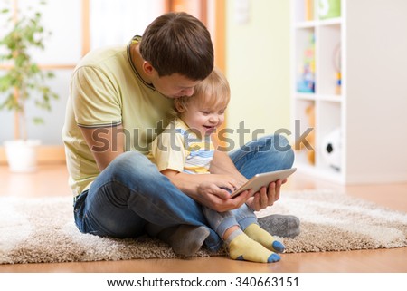 Young man and his son kid playing with tablet computer indoors